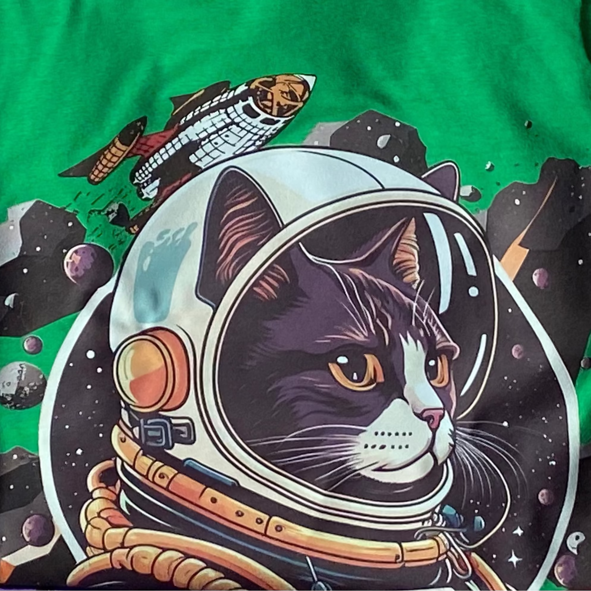 Stack of colorful t-shirts with various designs, including a green one with a space-themed graphic by PrintPony.